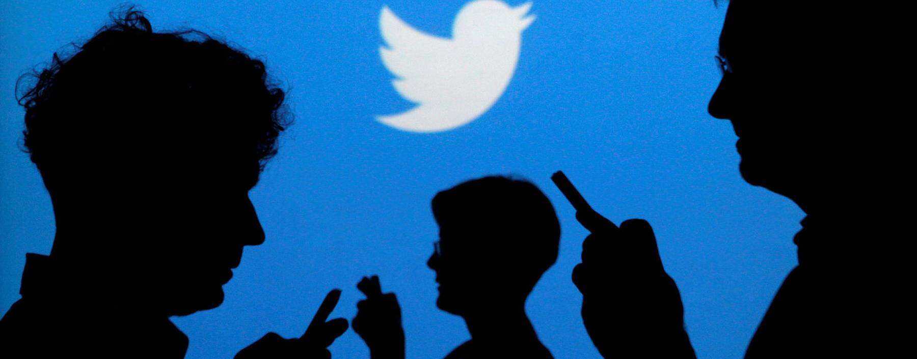 FILE PHOTO - People holding mobile phones are silhouetted against a backdrop projected with the Twitter logo in Warsaw