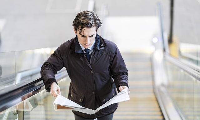 Businessman on escalator reading a newspaper model released Symbolfoto PUBLICATIONxINxGERxSUIxAUTxHU