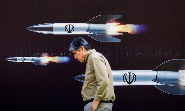 Passant in Teheran vor einem iranischen Propagandaplakat mit Raketen.