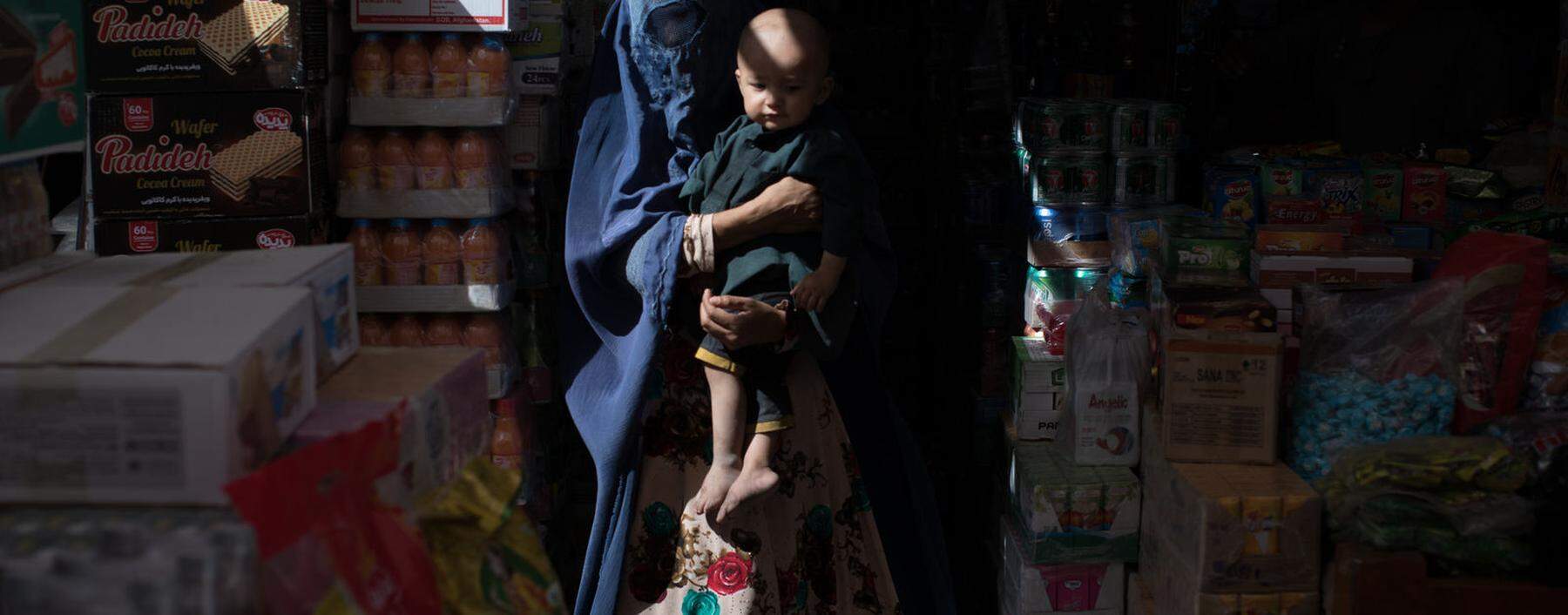 In Burka gehüllte Bettlerin mit Kind in einer Marktgegend in Mazar-i-Sharif, Nordafghanistan.