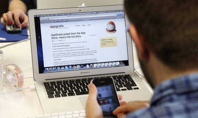An employee uses his Iphone as he works on a computer screen displaying the AppGratis blog in the offices of AppGratis company in Paris