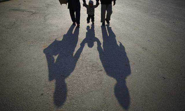 The shadow of a family is cast on the road as they walk along the deserted road while heading towards work during the general strike in Kathmandu