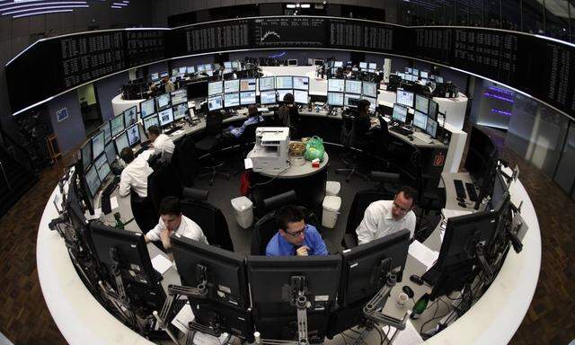 Traders are pictured at their desks in front of the DAX board at the Frankfurt stock exchange