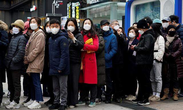 People wearing masks after the coronavirus outbreak wait in a line to buy masks in front of a department store in Seoul
