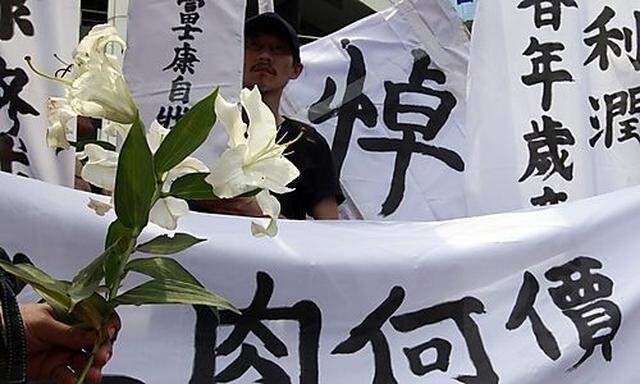 Labour union protester holds a flower to symbolise mourning in front of banners during a protest outs