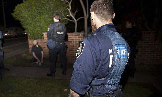 AFP handout shows Australian Federal Police officer and a New South Wales policeman standing near a suspect who was detained during a raid on a house in western Sydney