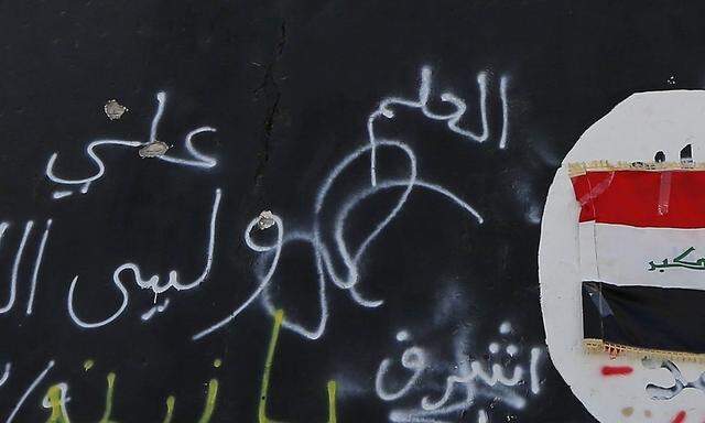 A member of militias known as Hashid Shaabi stands next to a wall painted with the black flag commonly used by Islamic State militants, in the town of al-Alam