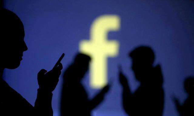 FILE PHOTO: Silhouettes of mobile users are seen next to a screen projection of Facebook logo in this picture illustration