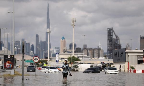 Ein Mann watet in der überschwemmten Stadt Dubai im Wasser, im Hintergrund der Burj Khalifa.
