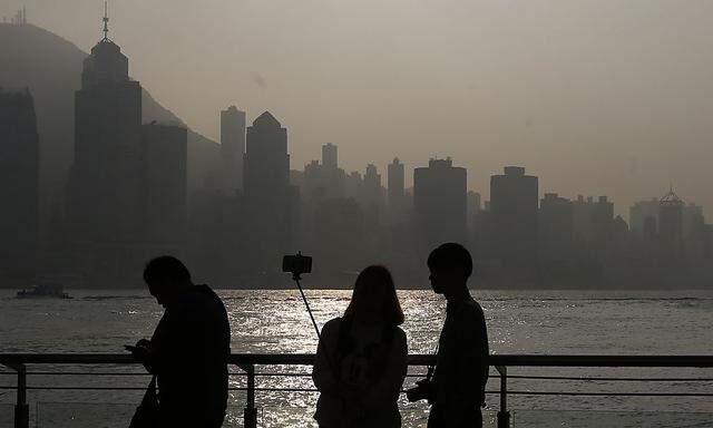 A couple takes a selfie during sunset on a waterfront facing the financial Central district in Hong Kong