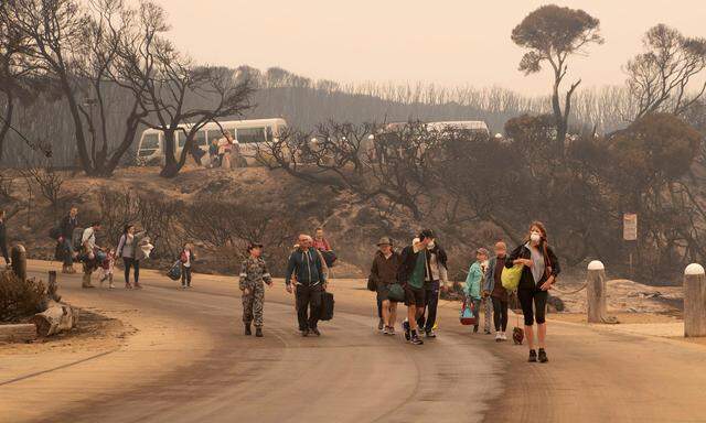 An image obtained on January 3, 2020, shows bushfire evacuees walking down to the beach to board vessels and be ferried out to HMAS Choules at Mallacoota