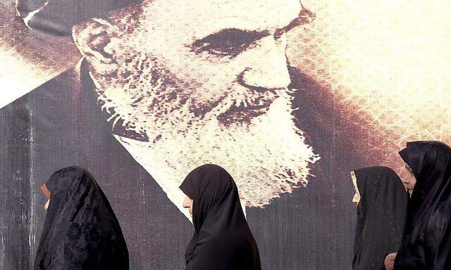 Iranian women walk past a poster of Iran's late leader Ayatollah Ruhollah Khomeini during the anniversary ceremony of Iran's Islamic Revolution in Behesht Zahra cemetery, south of Tehran