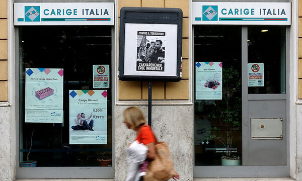 FILE PHOTO: A woman walks past a Carige bank in Rome, Italy