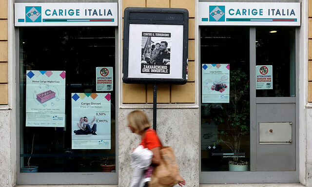 FILE PHOTO: A woman walks past a Carige bank in Rome, Italy