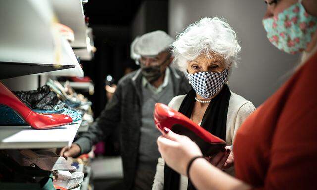 Senior couple wearing face mask being helped by a saleswoman while shopping for shoes in a thrift store