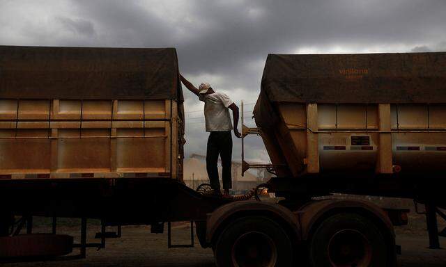 A Brazilian truck driver covers his face to protect himself from dust as he waits to unload his cargo of cereal grain in Alto de Araguaia