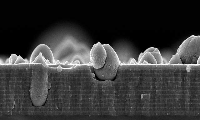 Eine wenige Mikrometer starke Dünnschicht unter dem Rasterelektronenmikroskop: Die dickeren Lagen bestehen aus Titanaluminiumnitrid, die dünneren aus Molybdän-Silizium-Bor. Die tropfenförmigen Teile sind ungewollt entstandene Defekte.