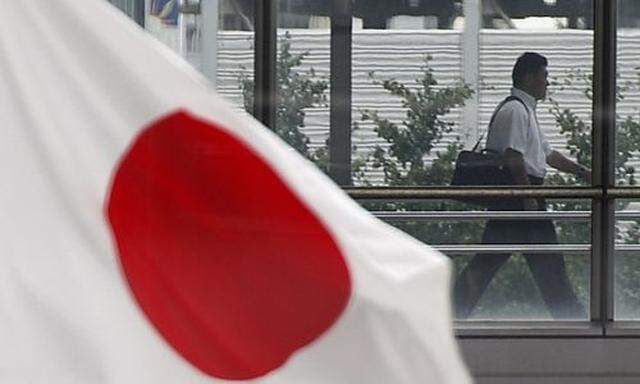 A businessman walks past a Japanese national flag in Tokyo