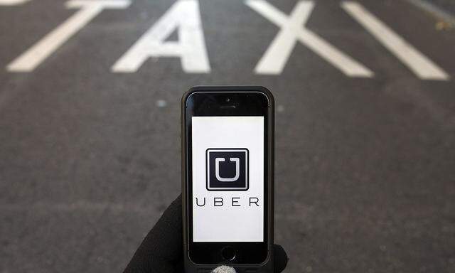 Photo illustration of logo of car-sharing service app Uber on a smartphone over a reserved lane for taxis in a street in Madrid