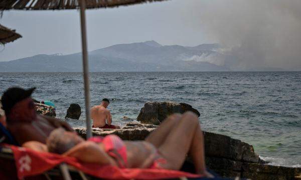 Urlauber nehmen ein Sonnenbad an der albanischen Küste, während auf der nahen griechischen Insel Korfu ein Brand wütet.