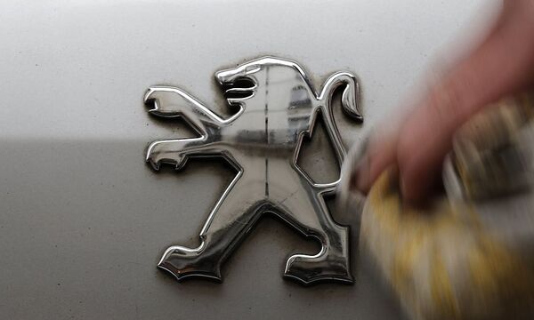 A man cleans a company logo on a Peugeot car parked in Paris