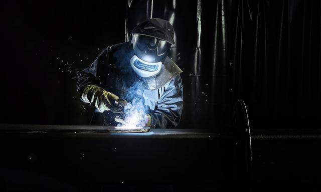Industrial worker in protective clothing welding metal with welding torch