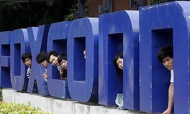 Workers look on from a Foxconn logo near the gate of a Foxconn factory in the township of Longhua