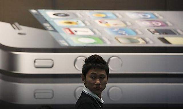 A man stands next to a giant advertisement for an iPhone 4 displayed at a shop in Bangkok