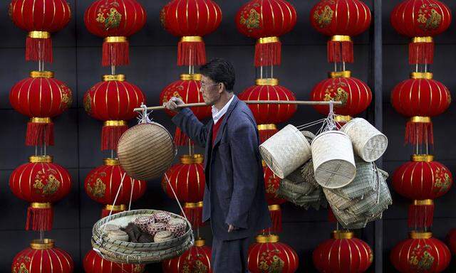 File photo of a basket vendor walking past red lanterns serving as decorations to celebrate the new year outside a shopping mall in Kunming