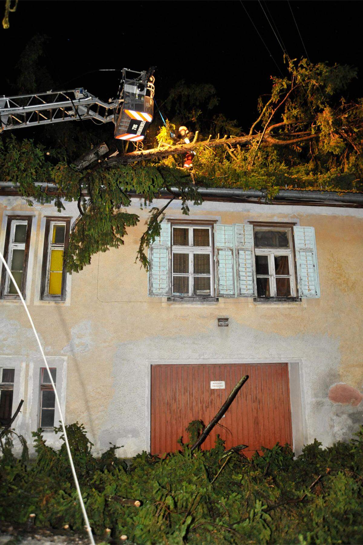Tirol: Einsatzkräfte der Feuerwehr befreien ein Hausdach von einem umgestürzten Baum.