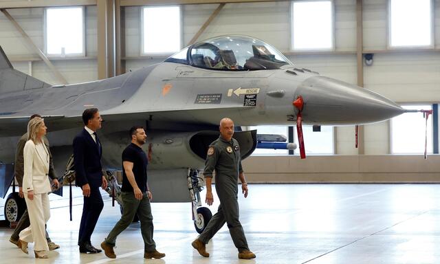 Wolodymyr Selenskij (Mitte) hinter dem holländischen Luftwaffenchef, General André Steur, und vor Premier Mark Rutte in Eindhoven, dahinter eine F-16. 