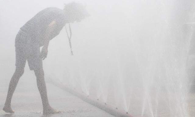 Ein Mann kühlt sich angesichts der Rekordhitze an einem Wasserschlauch
