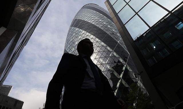 A man is silhouetted, as he passes the Swiss RE building in the City of London