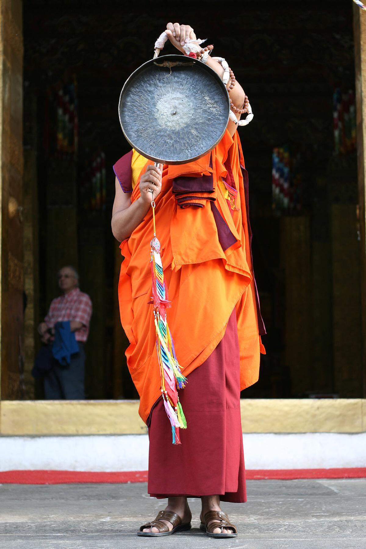 Ein Mönch in der traditionellen orange-roten Robe schlägt im Dzong von Punakha einen Gong. Bhutan ist ein großteils buddhistisches Land, die Religion ist auch in der Politik ein wichtiger Faktor.