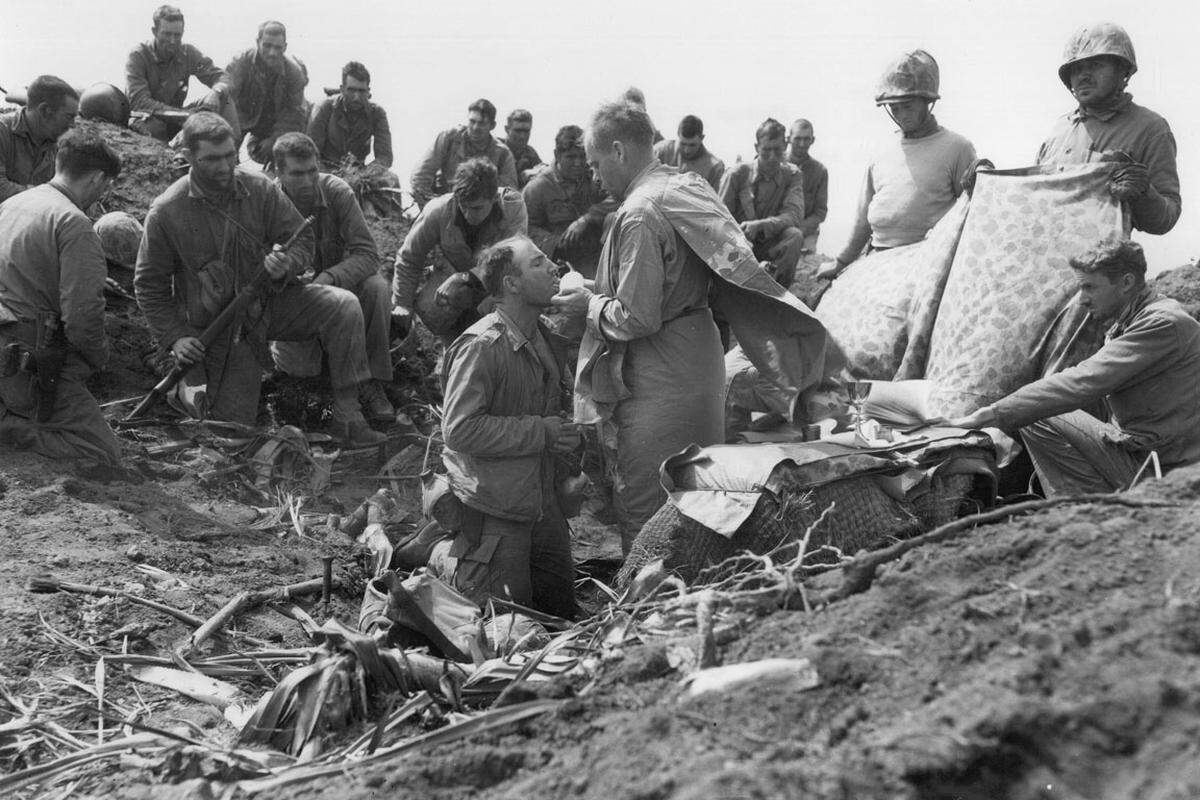 Der Bataillonsführung ist die Flagge allerdings zu klein, ein Trupp von Soldaten soll die Flagge austauschen. Sechs Soldaten machen sich, von Kriegsfotograf Joe Rosenthal begleitet, auf den Weg. Dieser macht vom Austausch der Fahne 18 Fotos. Im Bild: Ein katholischer Geistlicher feiert am Gipfel des eroberten Suribachi eine Messe.