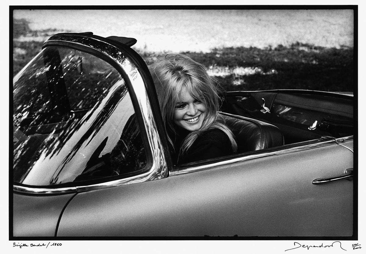 ... Brigitte Bardot grinst amusiert aus einem Cabrio, ...  Im Bild: Raymond Depardon: Brigitte Bardot, 1960. © Raymond Depardon/Magnum Photos 