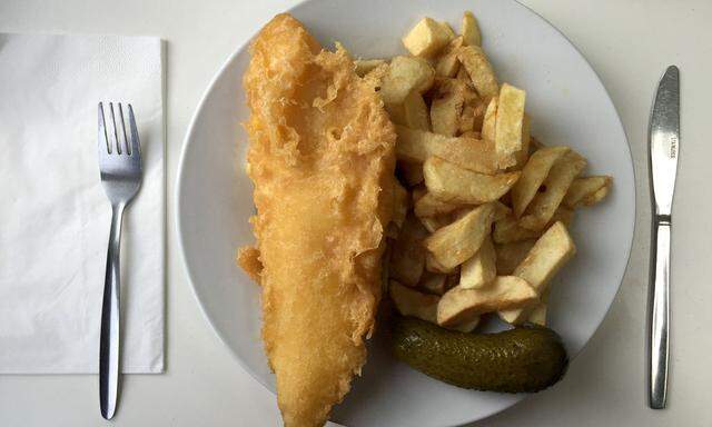 A plate of traditional fish and chips with a gherkin on a table in a seafront fish and chip shop in Brighton