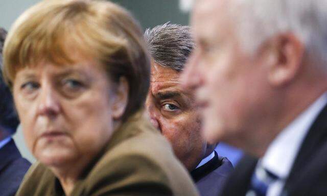 German Economy Minister Gabriel peers between Chancellor Merkel and Bavarian state premier and leader of the Christian Social Union Seehofer during a news conference at the Chancellery in Berlin