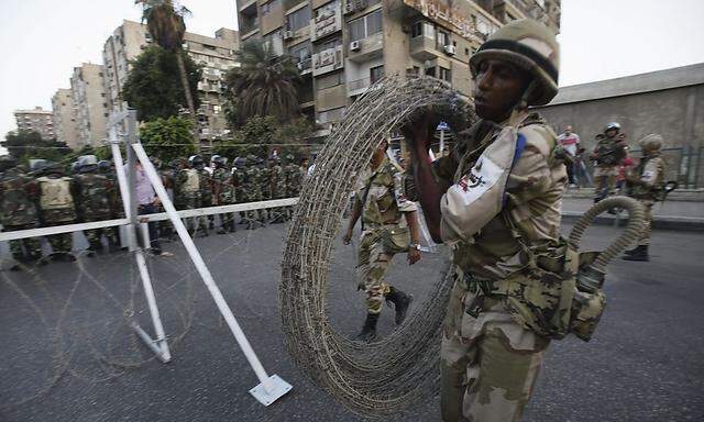 A soldier carries barbed wire fencing near army soldiers taking positions in front of protesters who are against Egyptian President Mursi, near the Republican Guard headquarters in Cairo