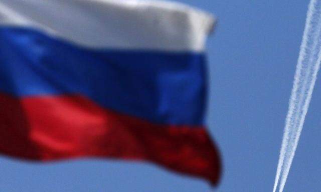 A contrail left by a passenger plane is seen behind a Russian state flag as it passes over the Siberian city of Krasnoyarsk