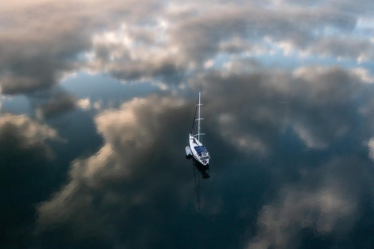 10. August. Dieses Luftbild zeigt ein Segelboot, das in der Bucht von Phaeton vor Anker liegt, während die Sonne über dem östlichen Teil der Insel Tahiti in Französisch-Polynesien aufgeht.