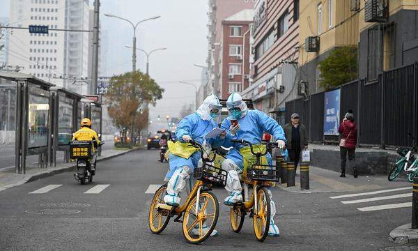 Mitarbeiter des Gesundheitswesens in persönlicher Schutzausrüstung, die Tupfer und Röhrchen zum Testen des Coronavirus Covid-19 tragen, sind am 24. November 2022 auf Fahrrädern auf einer Straße in Peking zu sehen.