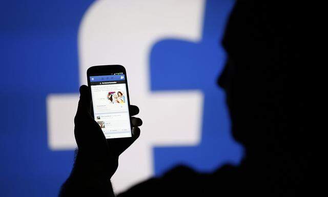 A man is silhouetted against a video screen with an Facebook logo as he poses with an Samsung S4 smartphone in this photo illustration taken in the central Bosnian town of Zenica