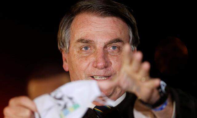Brazil's President Jair Bolsonaro holds his protective face mask after removing it while speaking with journalists as he arrives at Alvorada Palace, amid the coronavirus disease (COVID-19) outbreak, in Brasilia