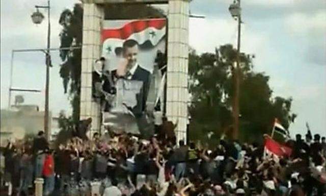 This still image taken from amateur video shows protesters defacing a giant poster of Syrias Presides Preside
