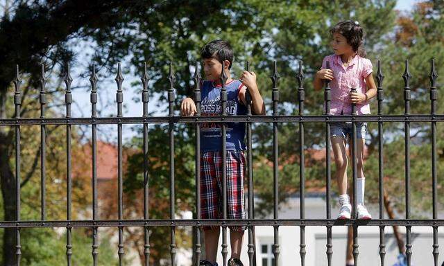 Children of asylum seekers stand behind the fence of an asylum processing center in Traiskirchen