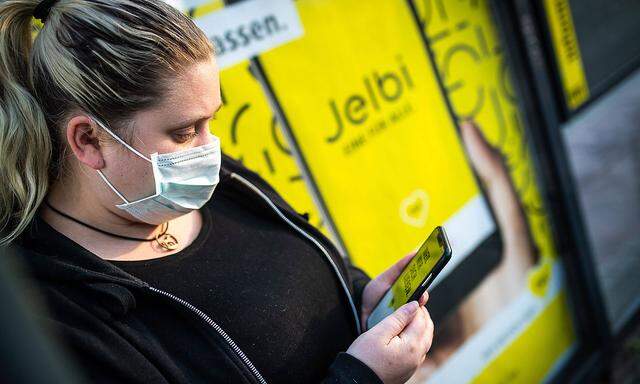Ein Frau mit einer Mund-Nasen-Maske nutzt die BVG -App auf ihrem Smartphone an einer Bushaltestelle der BVG in Berlin.
