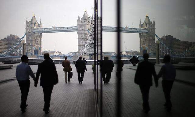 Pedestrians are reflected in glass fronted office buildings as they walk towards Tower Bridge on the south bank of the Thames, in central London