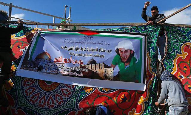 Palästinenser hängen ein Transparent mit dem Poträt des Attentäters in Ostjerusalem auf.