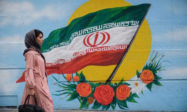 November 20, 2019, Tehran, Iran: An Iranian woman walks next to a wall painting of the Iranian national flag in Tehran,
